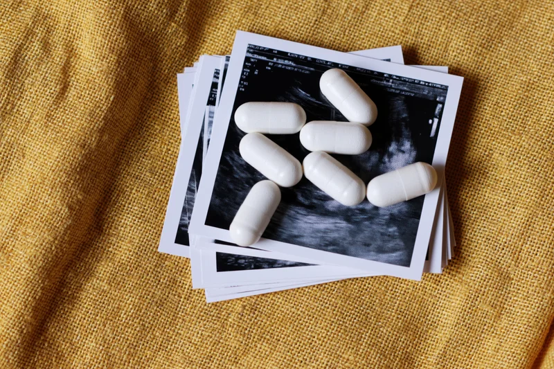 White supplement capsules scattered on top of ultrasound images of pregnancy on a yellow fabric surface