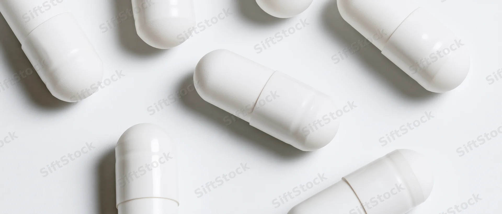 White pharmaceutical capsules scattered on a plain white surface