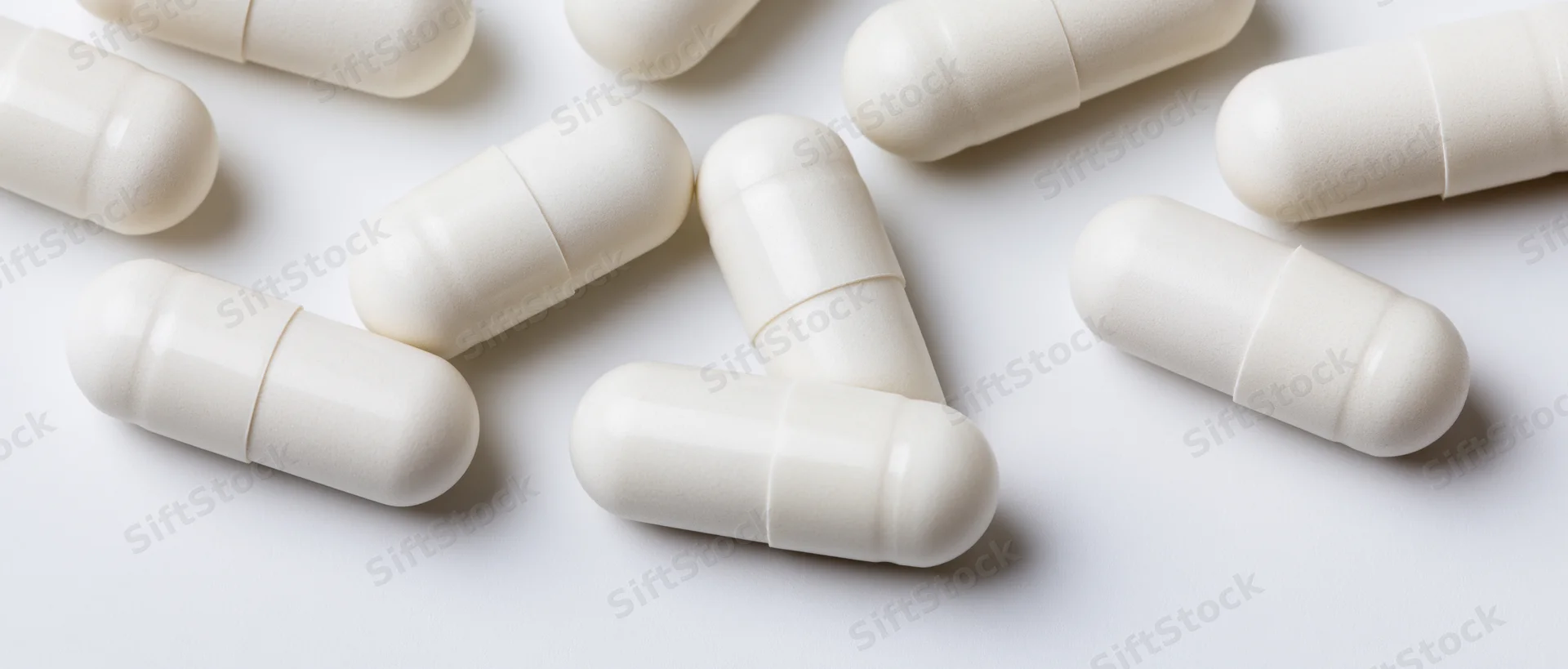 White pharmaceutical capsules scattered on a plain white surface