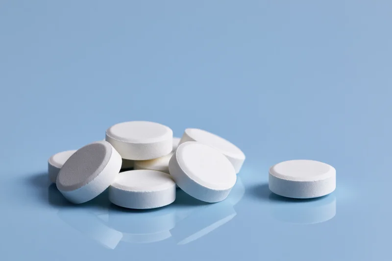 White round pharmaceutical tablets scattered on a reflective blue surface