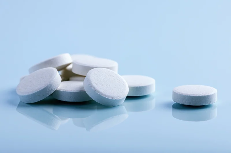 White round pharmaceutical tablets scattered on a reflective blue surface