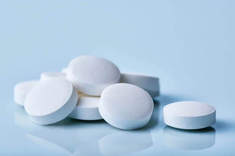 White round pharmaceutical tablets scattered on a reflective blue surface with copyspace