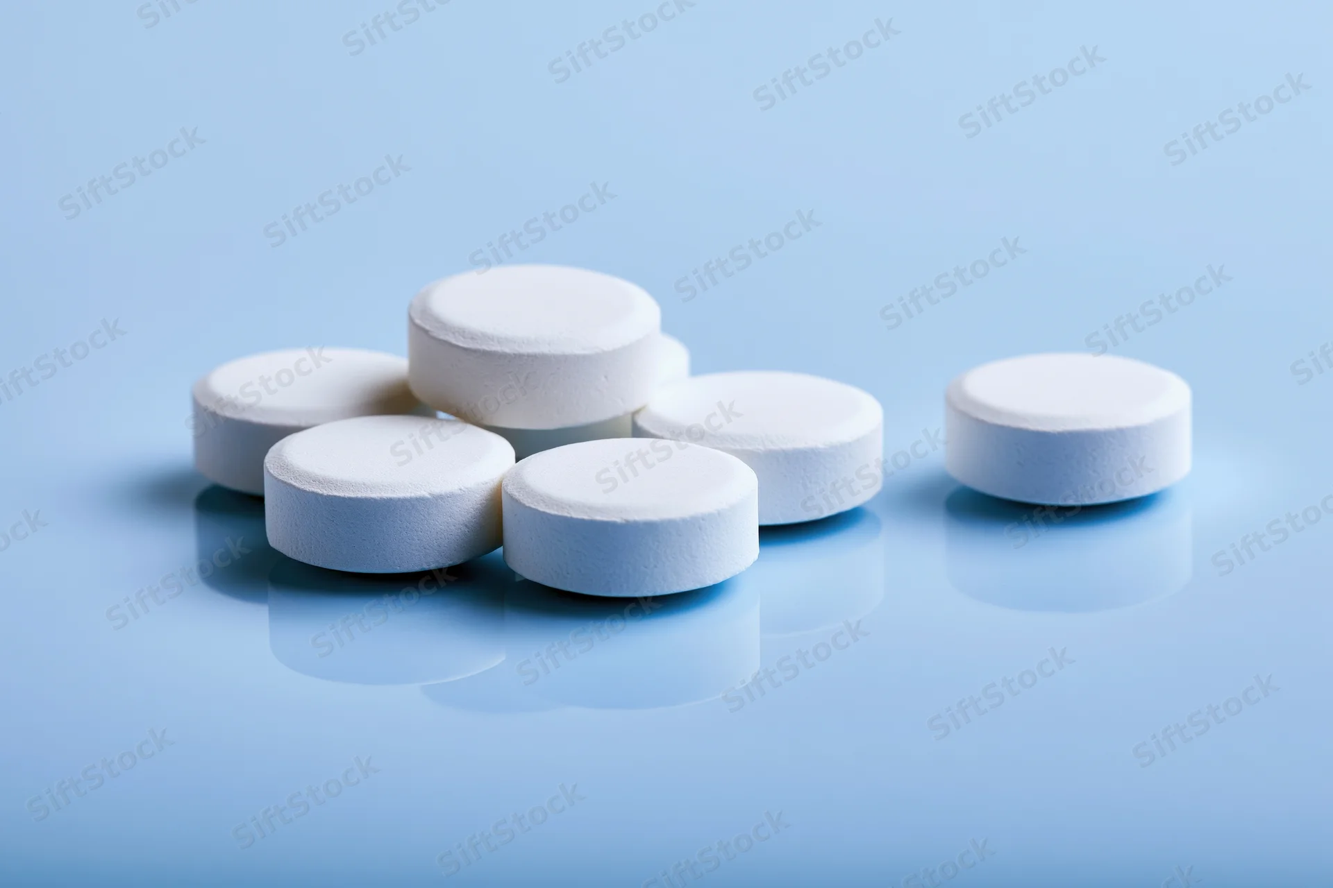 White round pharmaceutical tablets scattered on a reflective blue surface