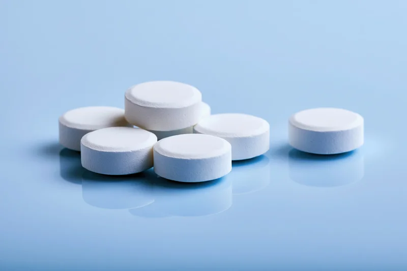 White round pharmaceutical tablets scattered on a reflective blue surface
