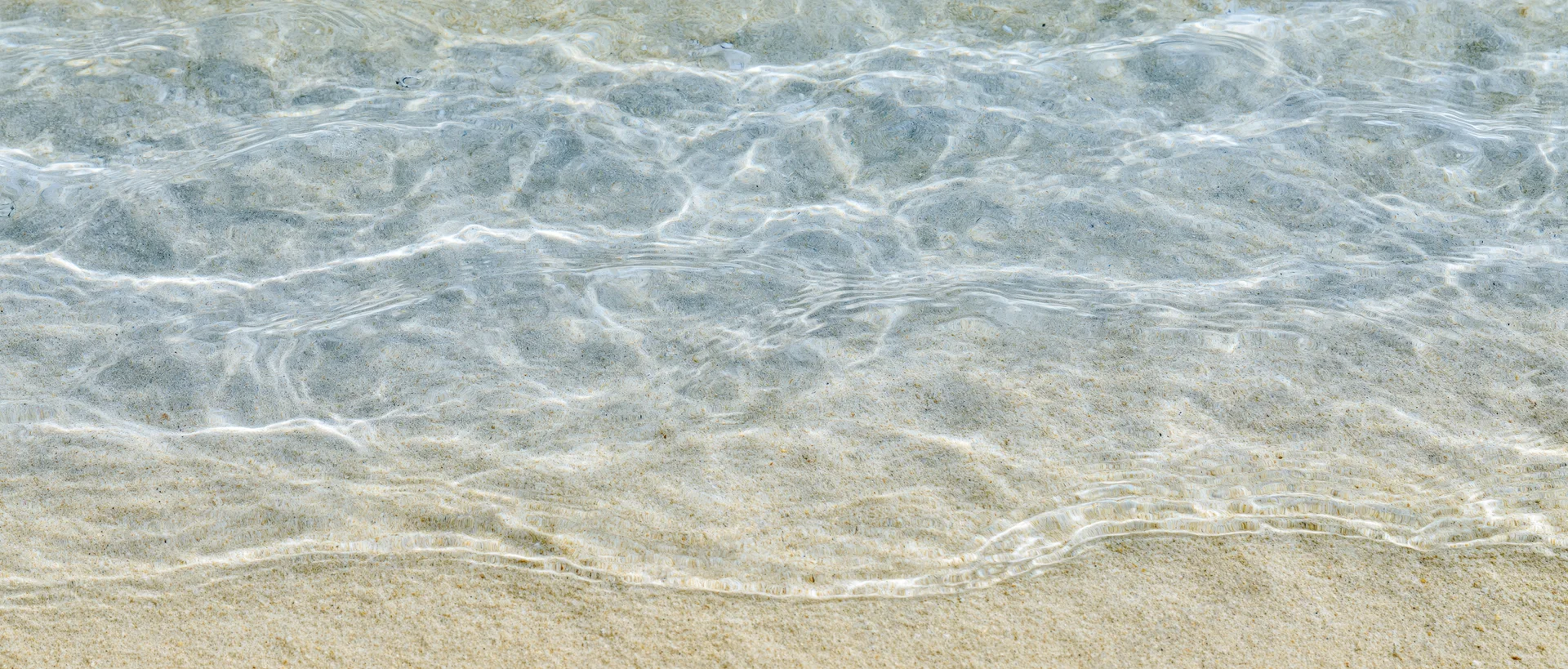 Clear shallow ocean water rippling over sandy seafloor at shoreline