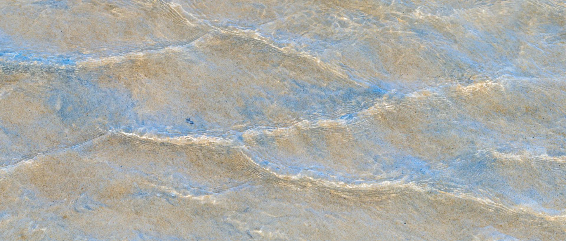 Shallow clear ocean water rippling over sandy seafloor from above