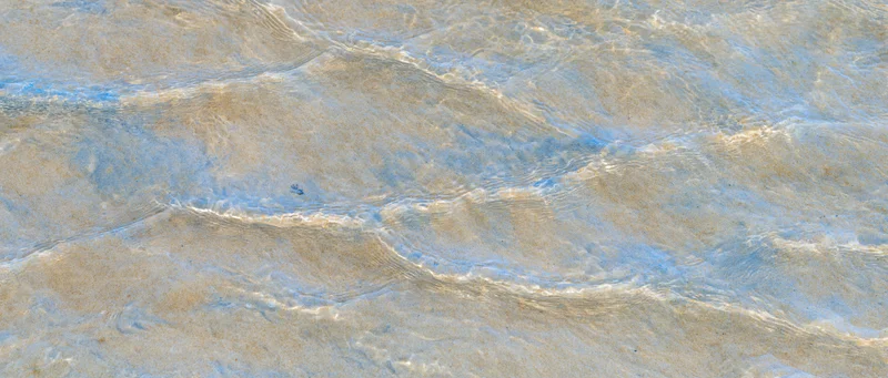 Shallow clear ocean water rippling over sandy seafloor from above