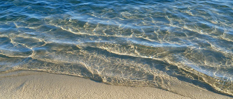 Shallow clear ocean water rippling over sandy seafloor at shoreline