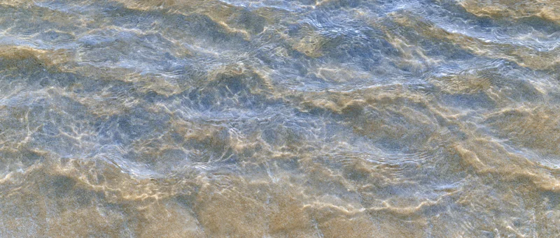 Shallow clear ocean water rippling over sandy seafloor top-down view