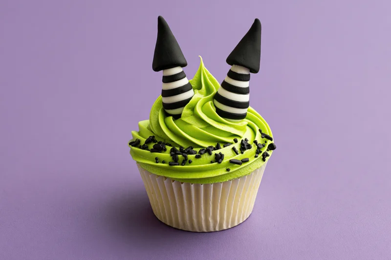 Halloween cupcake with green frosting and witch hat decorations on purple background