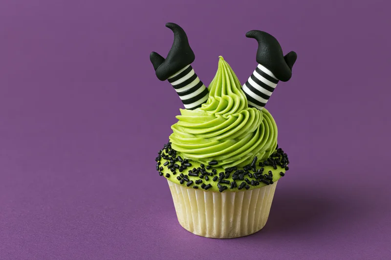 Halloween cupcake with green frosting and witch legs decoration on purple background
