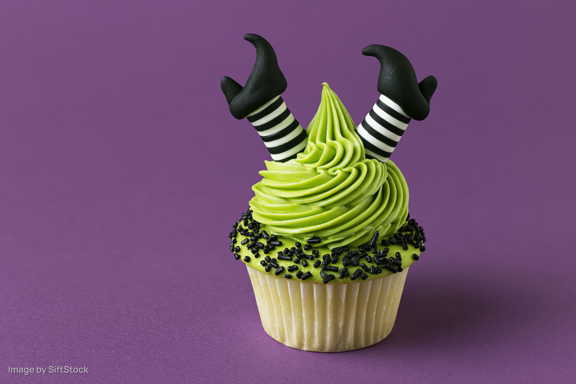 Halloween cupcake with green frosting and witch legs decoration on purple background