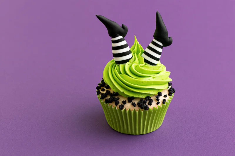 Halloween cupcake with green frosting and witch legs decoration on purple background
