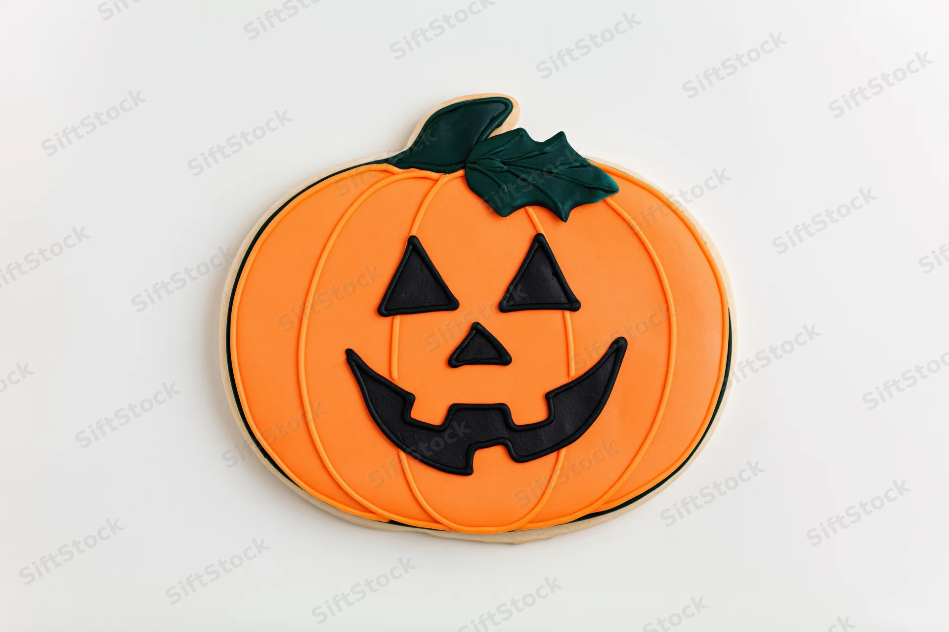 Halloween sugar cookie shaped like a jack-o-lantern with orange icing and black face details on white background