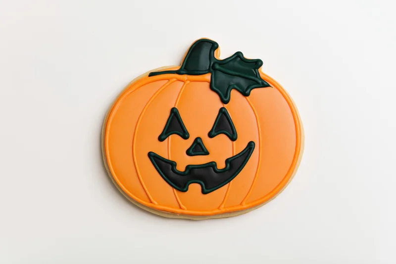 Halloween sugar cookie shaped as a jack-o-lantern with orange icing and black face details on white background