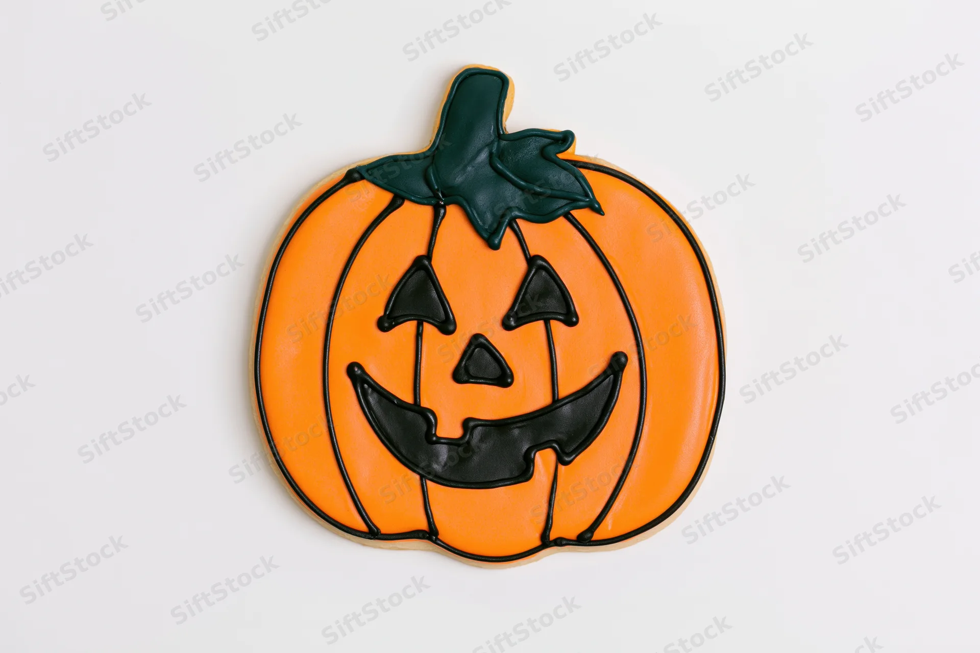 Halloween sugar cookie shaped like a jack-o-lantern with orange icing and black facial features on a white background