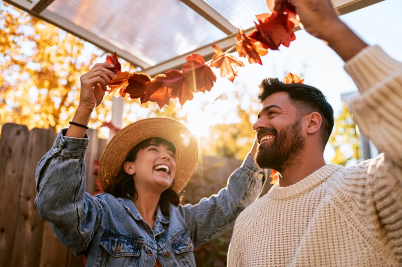 Couple laughing while hanging autumn leaf garland on outdoor patio