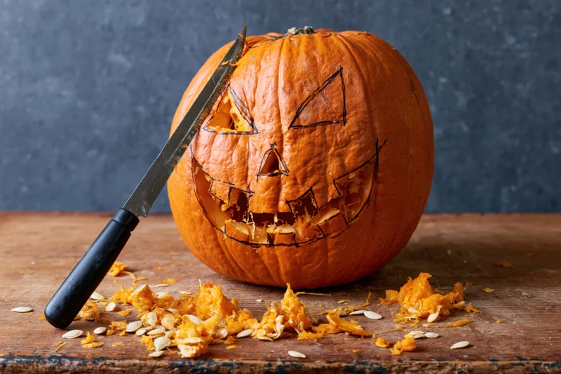 Carved pumpkin with knife on wooden table during halloween preparation