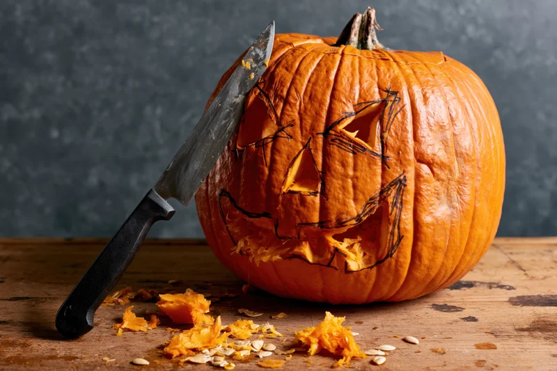 Carved pumpkin with knife on wooden table during halloween preparation