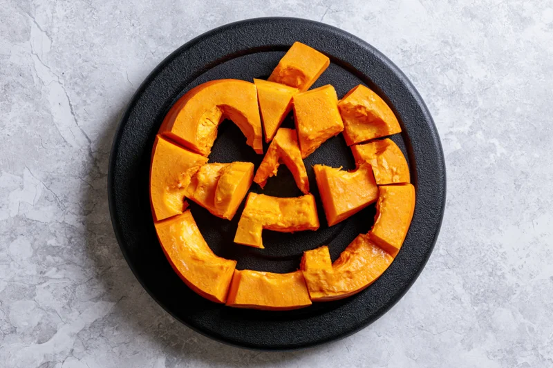 Carved pumpkin slices arranged in jack-o-lantern face on black circular plate on gray textured surface