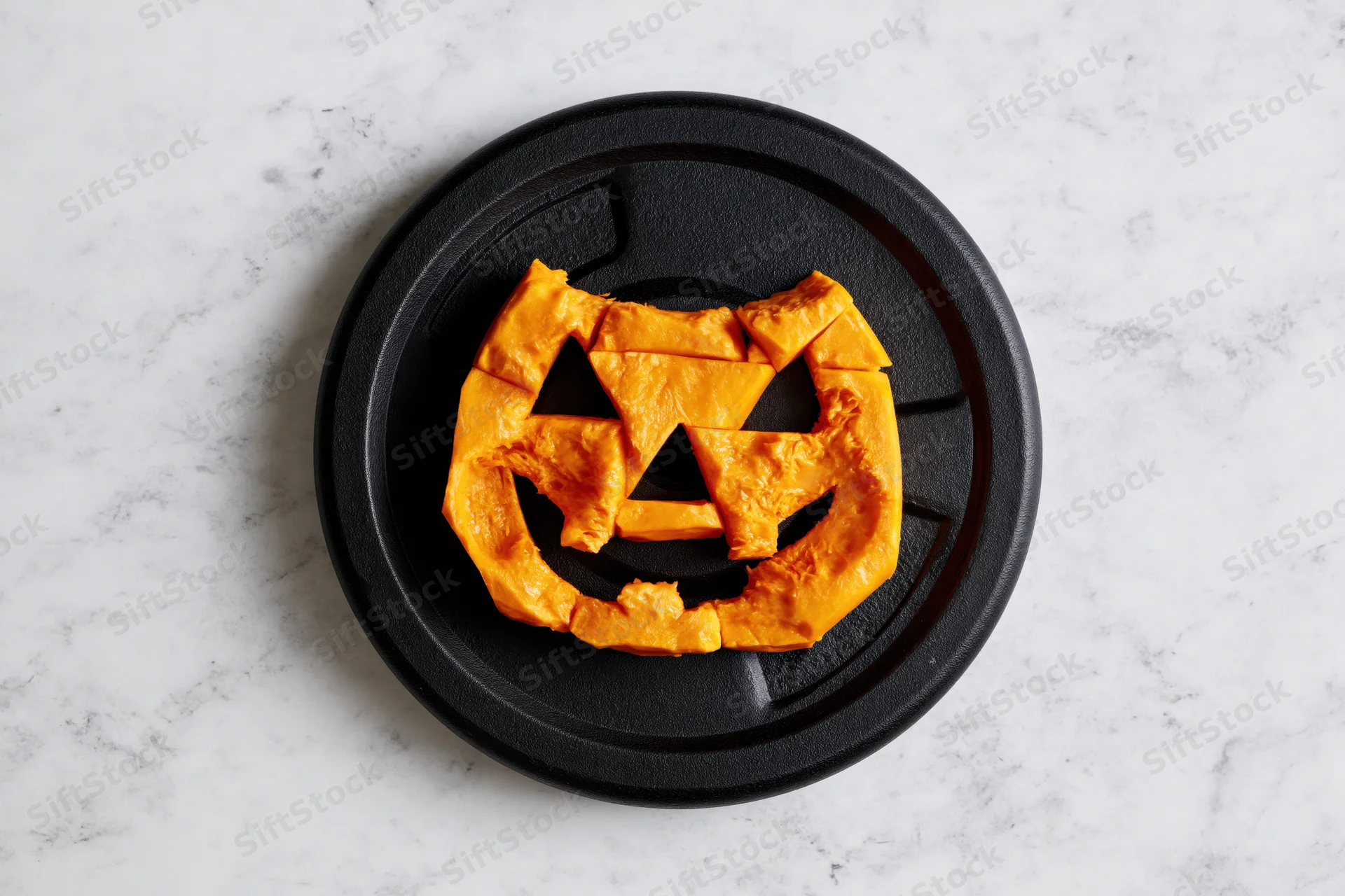 Carved orange pumpkin face on black gym weight plate on marble surface