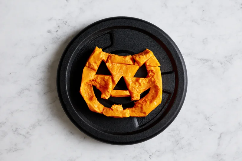 Carved orange pumpkin face on black gym weight plate on marble surface