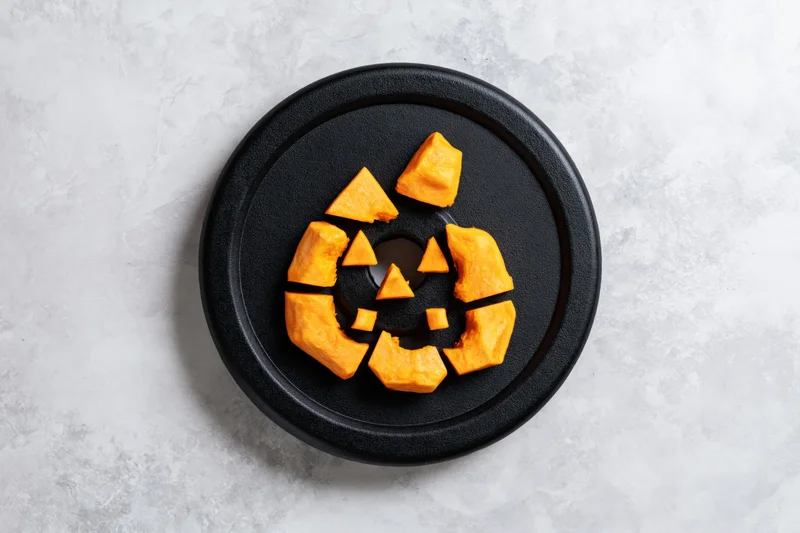 Carved pumpkin pieces arranged as a jack-o-lantern face on a black gym weight plate