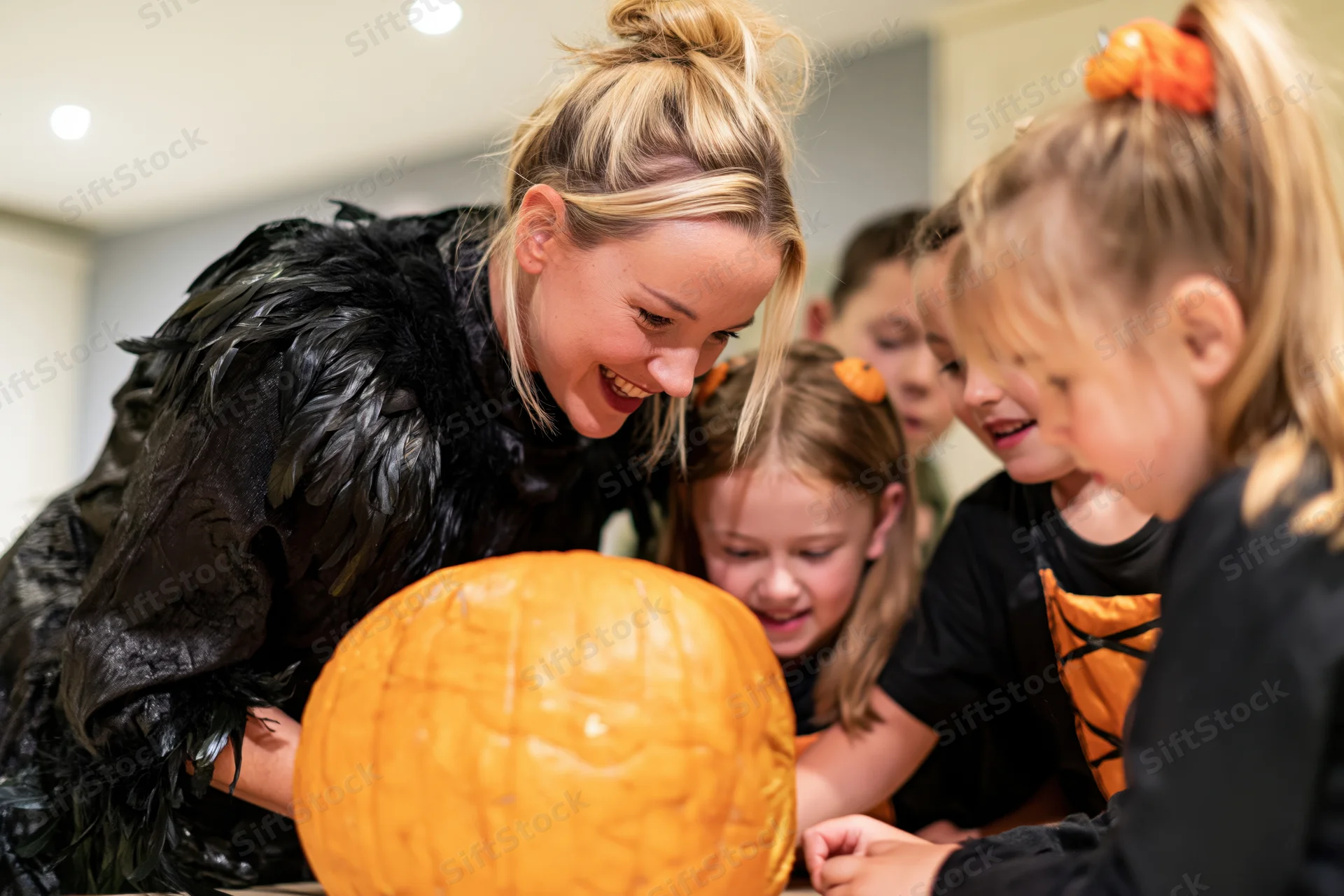 Woman in black feathered costume smiling while carving a pumpkin with children indoors