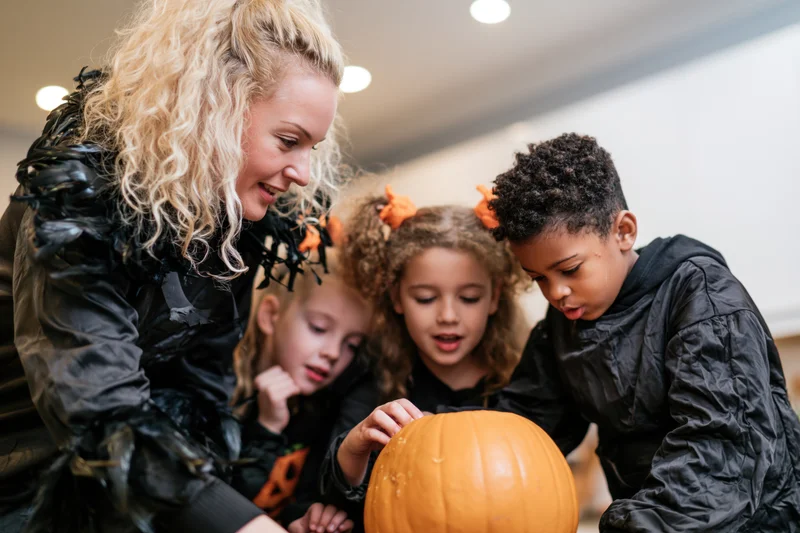 Woman and children carving a pumpkin together indoors for halloween