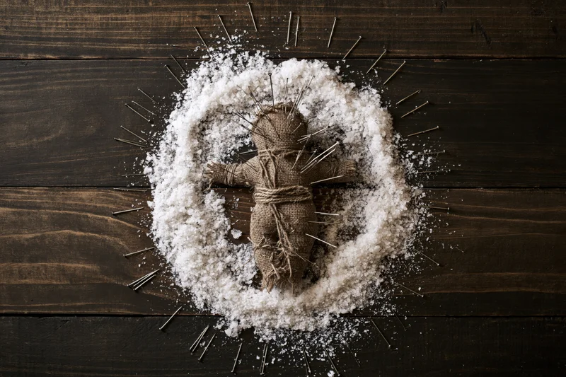Burlap voodoo doll bound with twine and stuck with pins arranged in a circle of salt on dark wooden surface