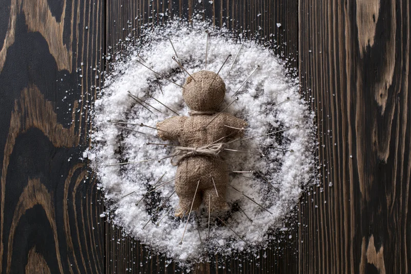 Burlap voodoo doll bound with twine and stuck with pins lying on snow-covered dark wooden surface