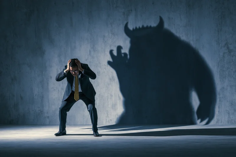 Businessman cowering in stress with monster shadow on concrete wall