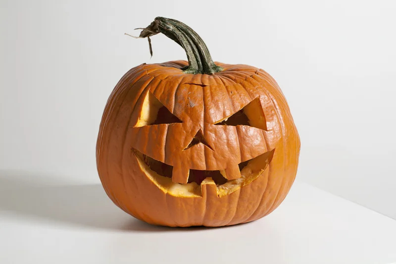 Carved pumpkin with angular face and stem on white surface