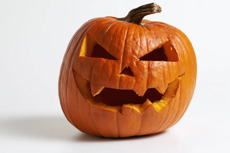Carved pumpkin with angular eyes and wide grin on white background