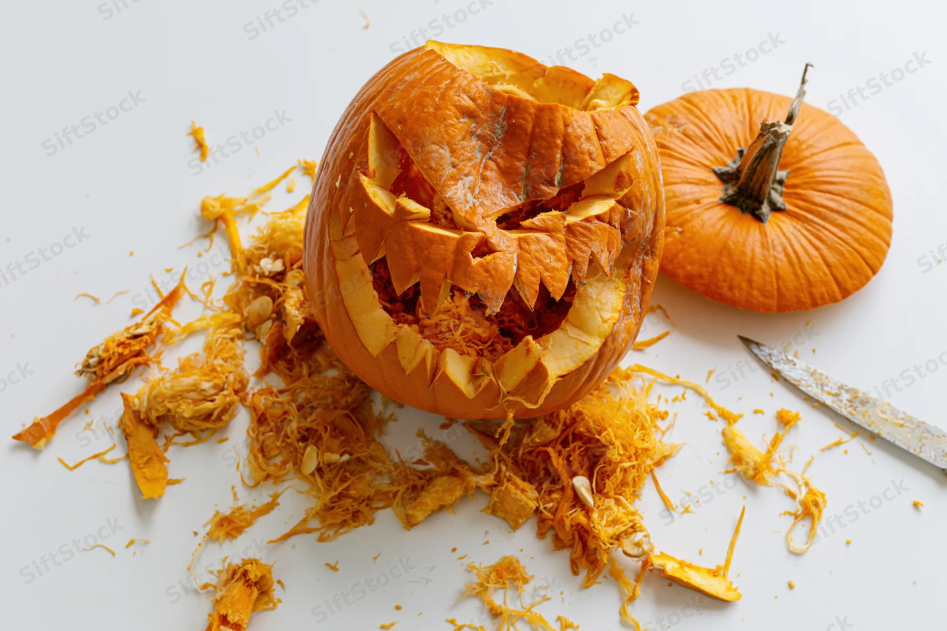 Carved pumpkin with jagged face and scattered pulp on white surface