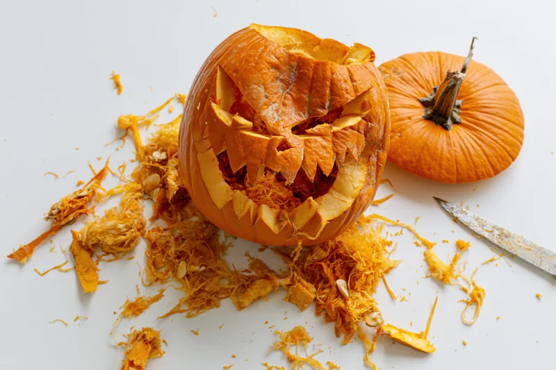 Carved pumpkin with jagged face and scattered pulp on white surface