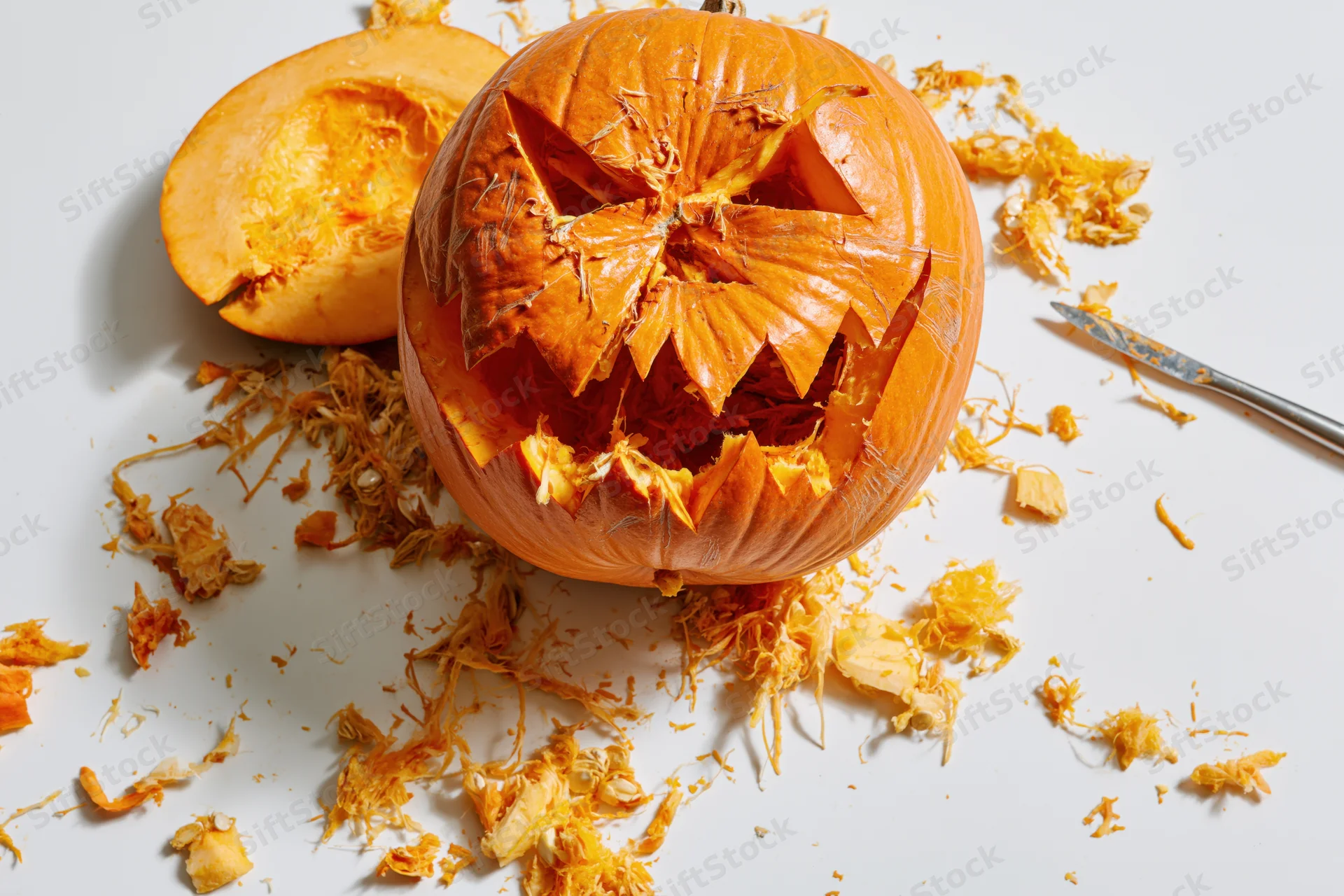 Carved pumpkin with jagged face and scattered pulp on white surface