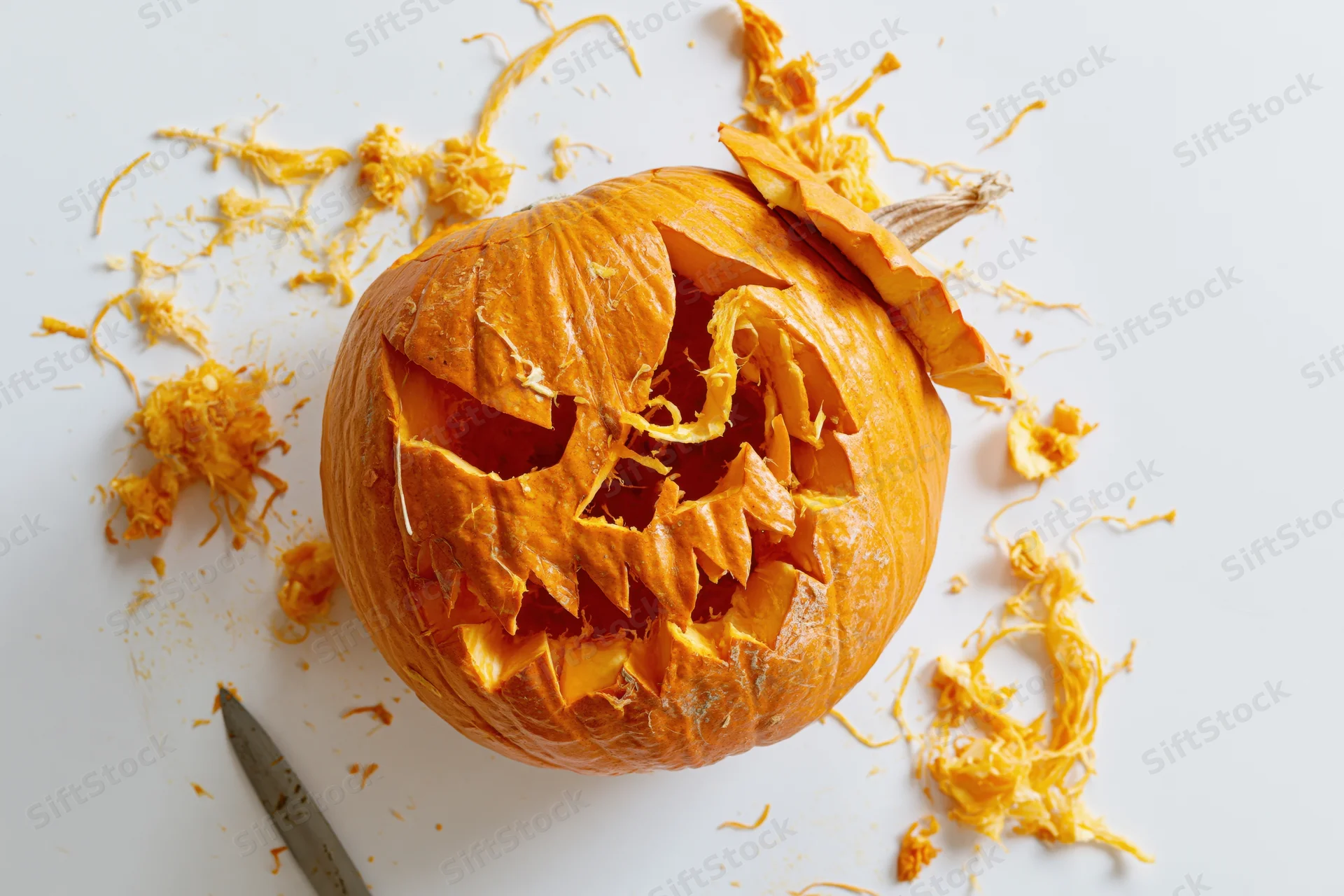 Carved pumpkin with jagged menacing face on white surface