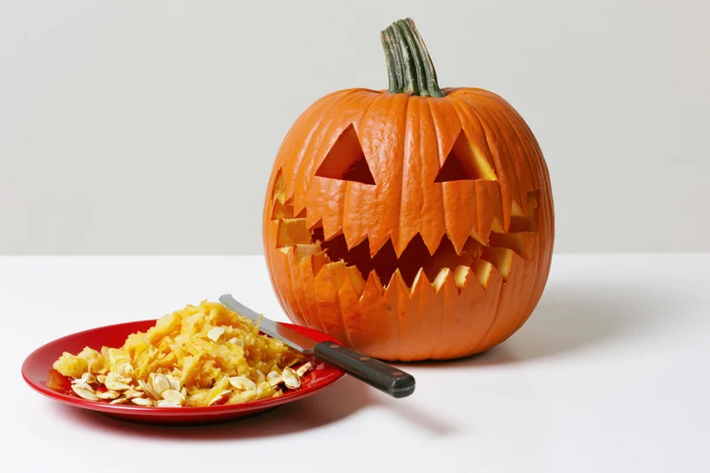 Carved pumpkin with jagged grin and removed pulp on a red plate beside a knife on a white surface