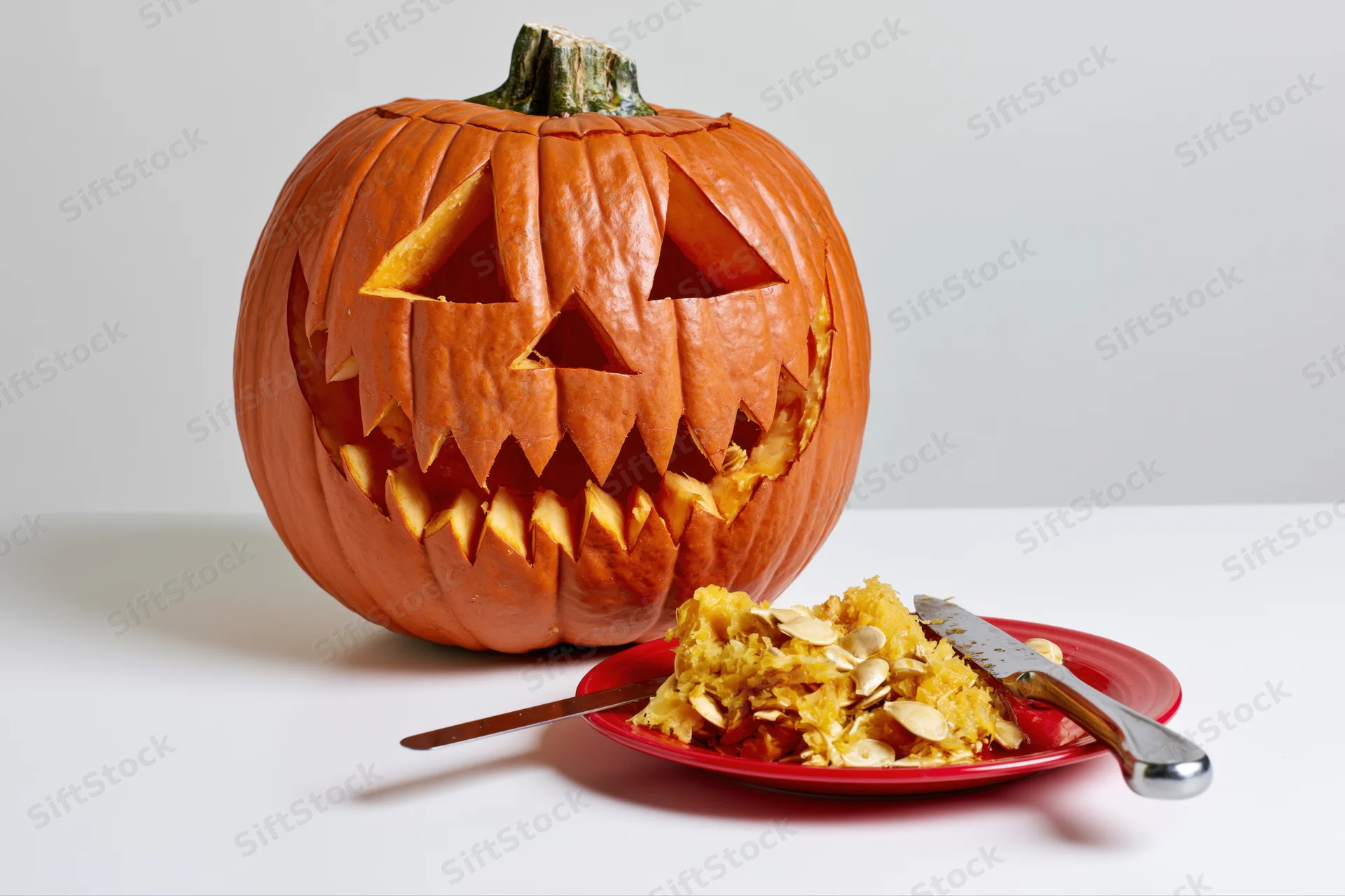Carved pumpkin with jagged grin and seeds on a red plate on white surface