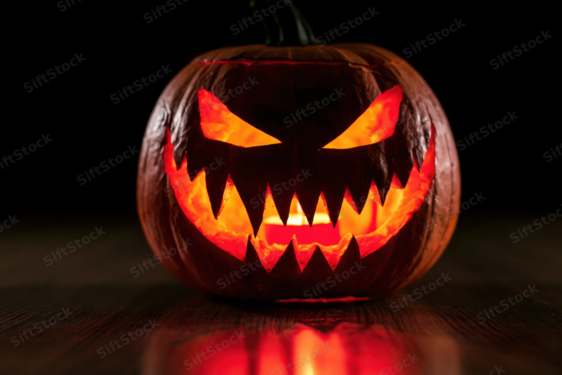 Carved pumpkin with glowing menacing face on dark wooden surface
