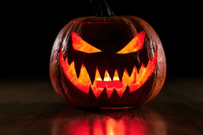 Carved pumpkin with glowing menacing face on dark wooden surface