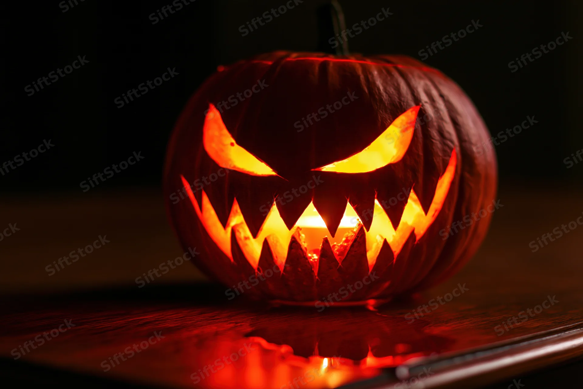 Carved pumpkin with jagged teeth and glowing eyes on a wooden table