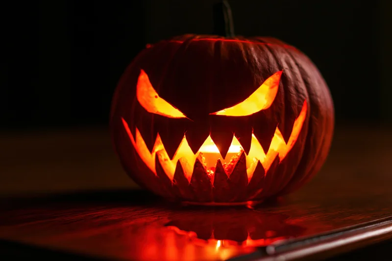 Carved pumpkin with jagged teeth and glowing eyes on a wooden table