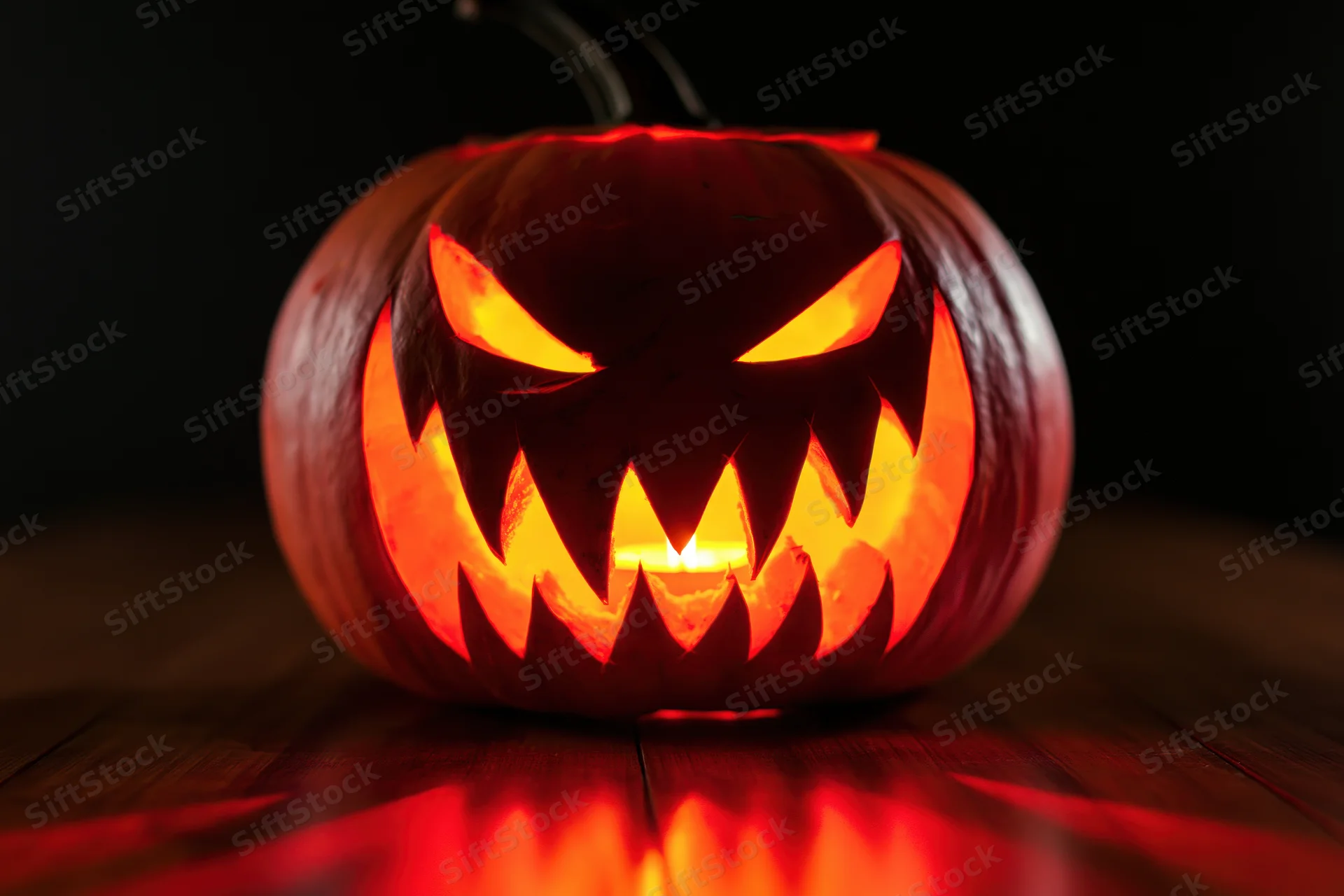 Carved pumpkin with jagged teeth and glowing eyes on wooden table