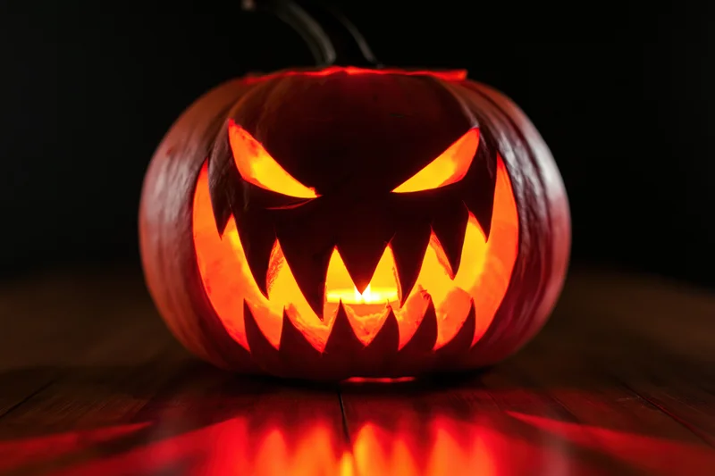 Carved pumpkin with jagged teeth and glowing eyes on wooden table