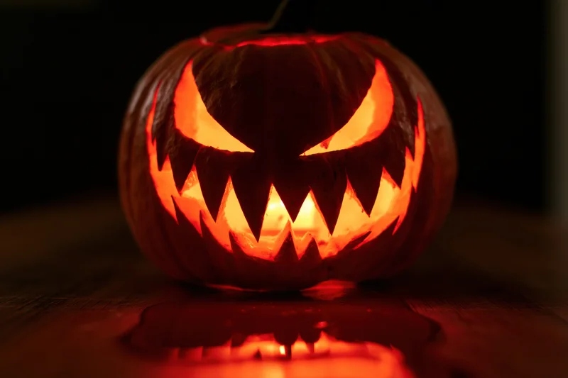 Carved pumpkin with jagged teeth and glowing eyes on wooden table at night