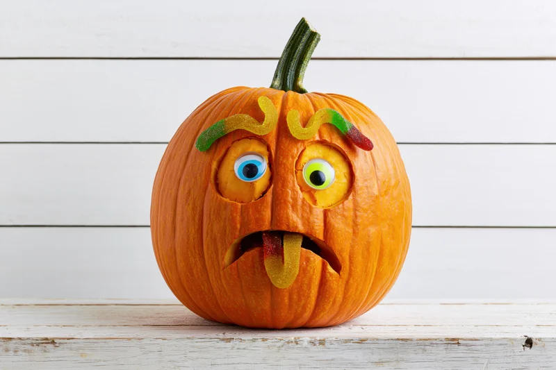 Carved pumpkin with gummy worm candies forming a playful face on a white wooden surface
