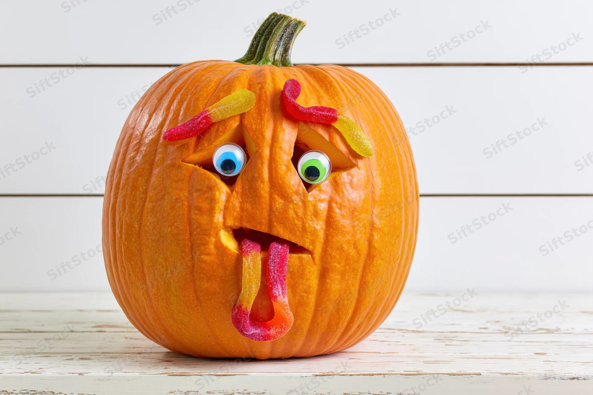 Carved pumpkin with gummy worm candies for halloween decoration on white wooden table