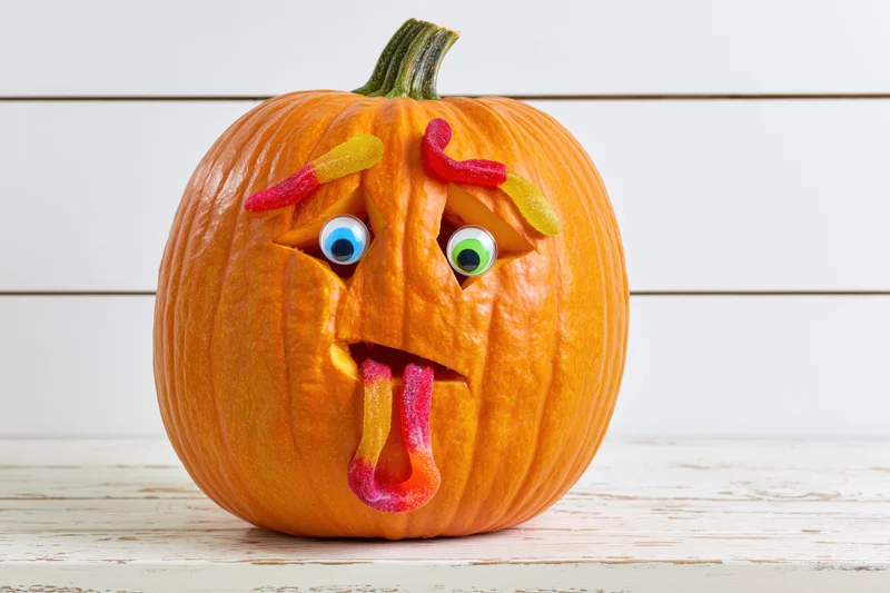 Carved pumpkin with gummy worm candies for halloween decoration on white wooden table